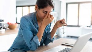 An image of a frustrated, grieving woman sitting over a laptop computer, to illustrate a Plannedgiving.Com blog post about the importance of women's estate planning.