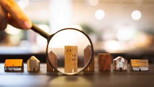 A picture of a magnifying glass focused on a toy wooden building, to illustrate a plannedgiving.com post encouraging nonprofits to accept gifts of real estate.