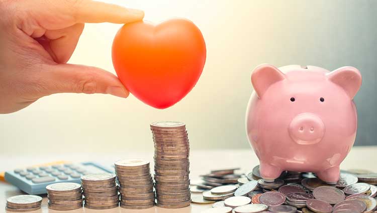 An image of a red heart held between fingertips over a stack of money from a nearby piggy bank, to accompany a PlannedGiving.Com blog on making a gift to a nonprofit from your retirement plan.