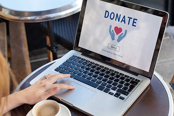 A picture of a woman with laptop and coffee cup making a planned giving donation online and considering a bequest.